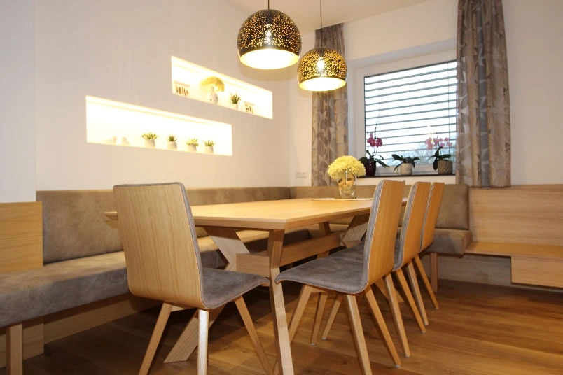 Holzesstisch mit Polsterstühlen und Hängelampe.