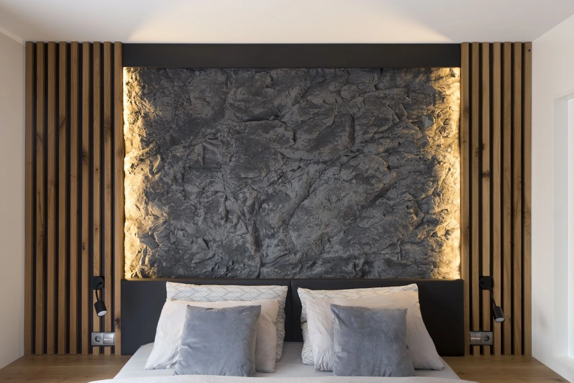 Gemütliches Doppelbett mit dunklem Kopfteil und indirekter Wandbeleuchtung.