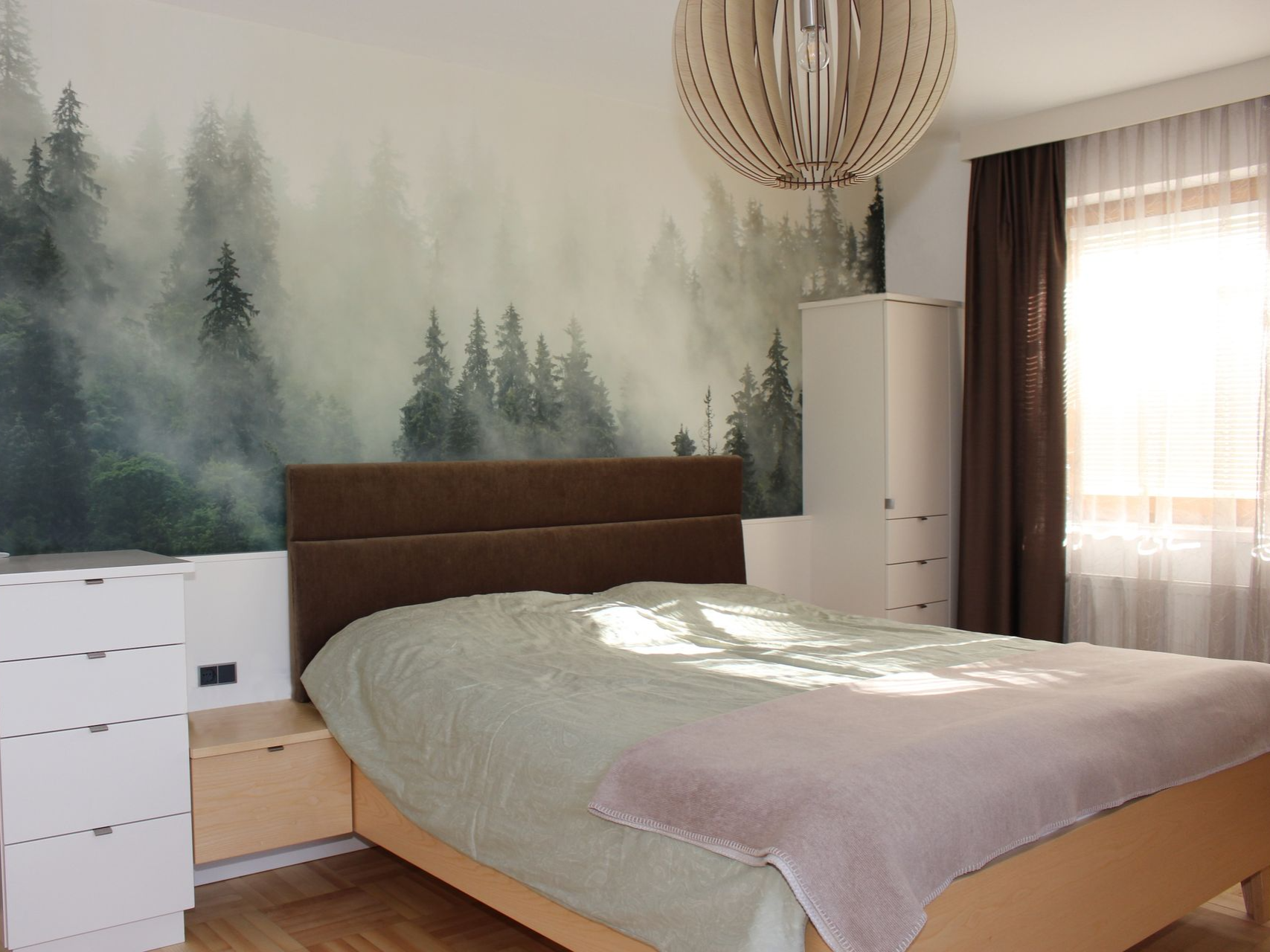 Gemütliches Bett vor Waldmotiv-Tapete im Schlafzimmer.