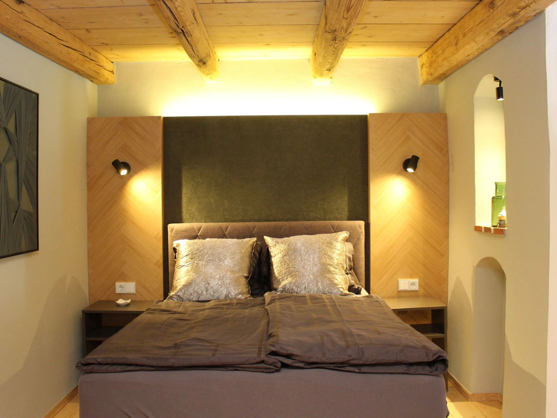 Boxspringbett und dahinter beleuchtete Wandpaneele in Fischgrätoptik.
